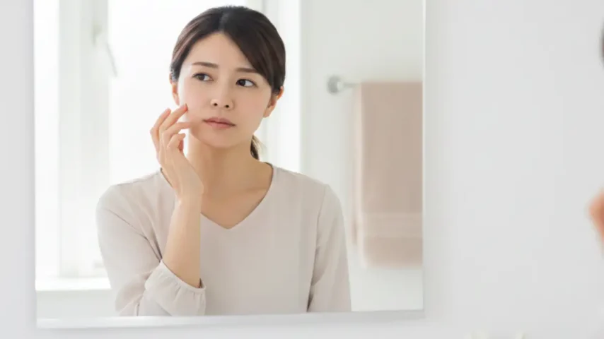 鼻に小さなほくろがある日本人女性が鏡の前で考え込む横長イメージ